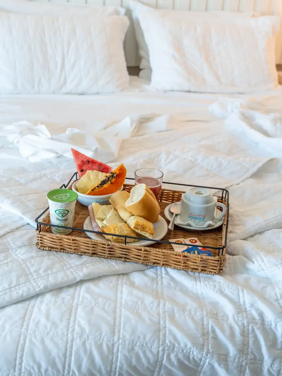 Bandeja de café da manhã sobre a cama, com frutas, pão, iogurte e xícara de café