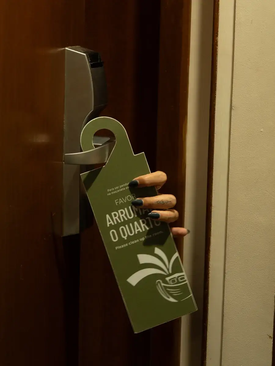 Aviso de porta verde com a marca do hotel, "Favor arrumar o quarto", pendurado na maçaneta