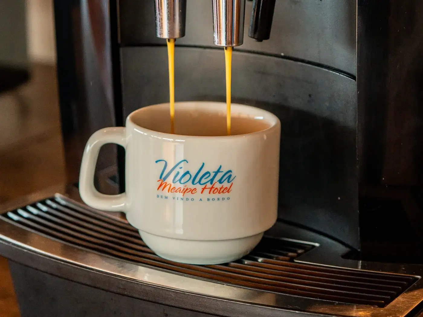 Xícara com a marca do hotel recebendo café na máquina