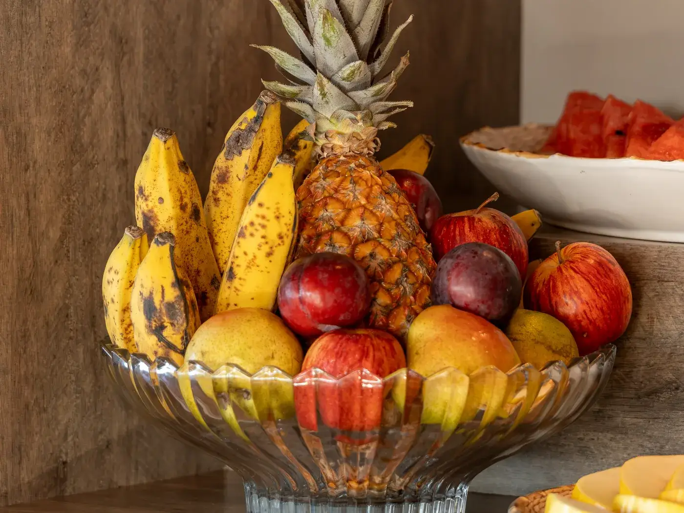 Fruteira do buffet com abacaxi, bananas, maçãs e ameixas