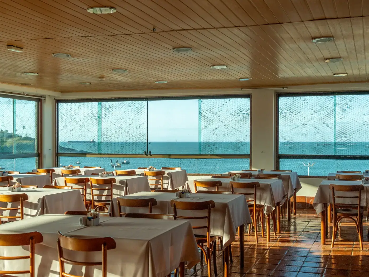 O salão do café visto de outro ângulo, com as mesas prontas e a enseada nas janelas
