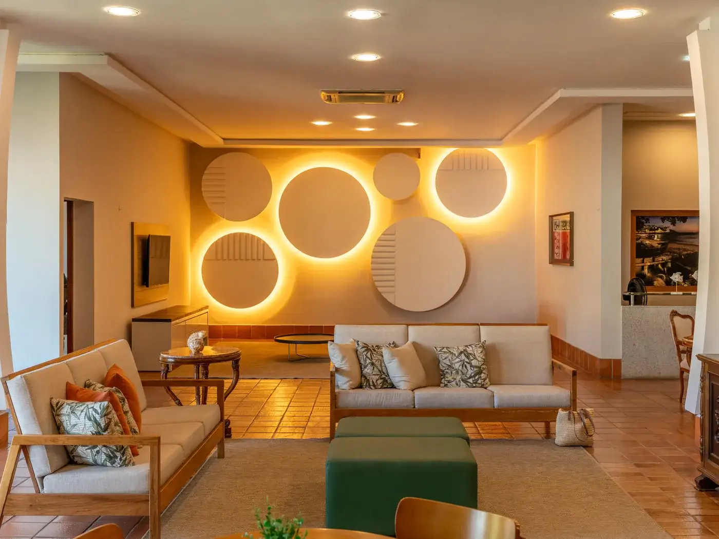 Sala de estar do hotel, com sofás, mesa de centro verde e painéis de luz redondos na parede