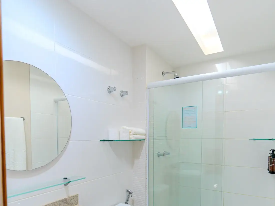 Banheiro do quarto, com box, bancada de madeira e espelho redondo