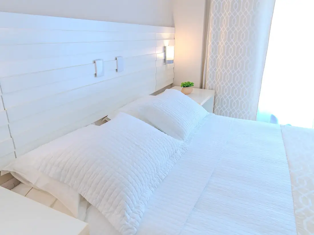 Cabeceira do quarto duplo, com as luminárias de leitura acesas e o enxoval branco