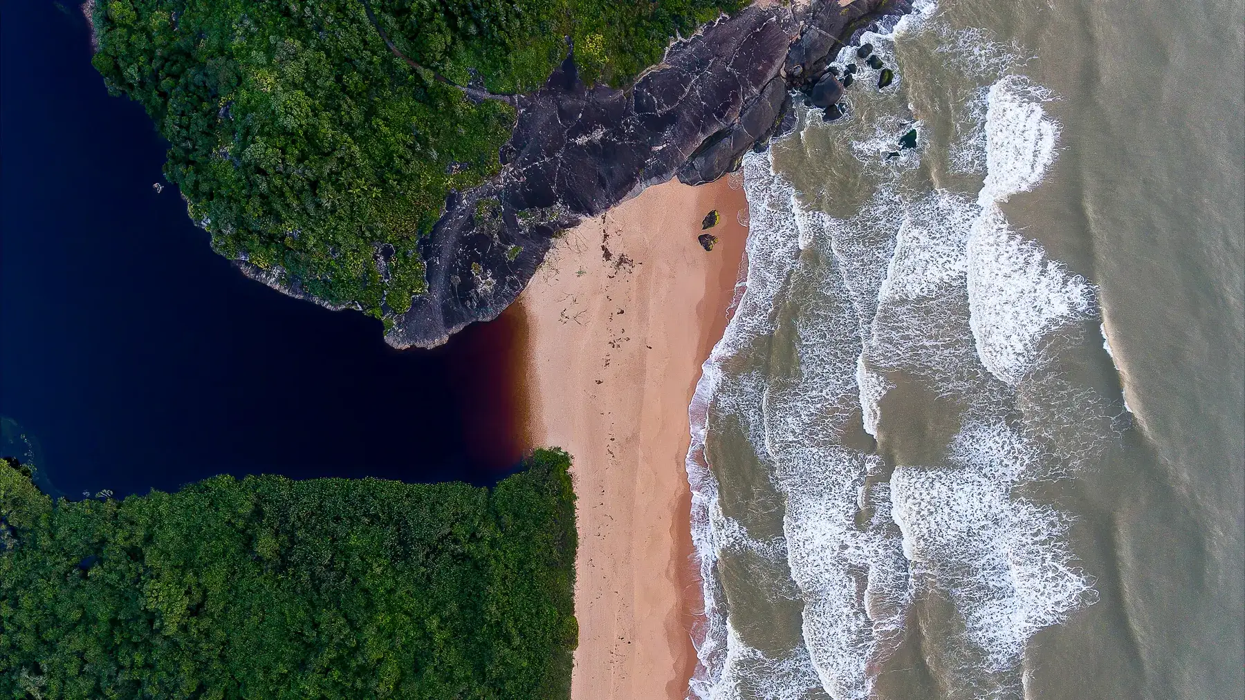 Vista de drone da praia de Caraís, com a lagoa escura de um lado e a arrebentação do outro