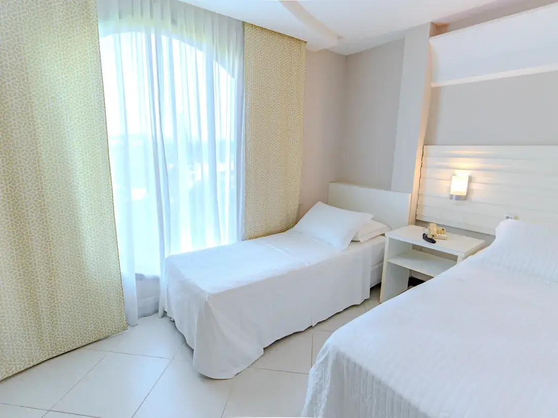 Quarto triplo com a cortina puxada, a cama de solteiro junto à janela e a queen ao lado